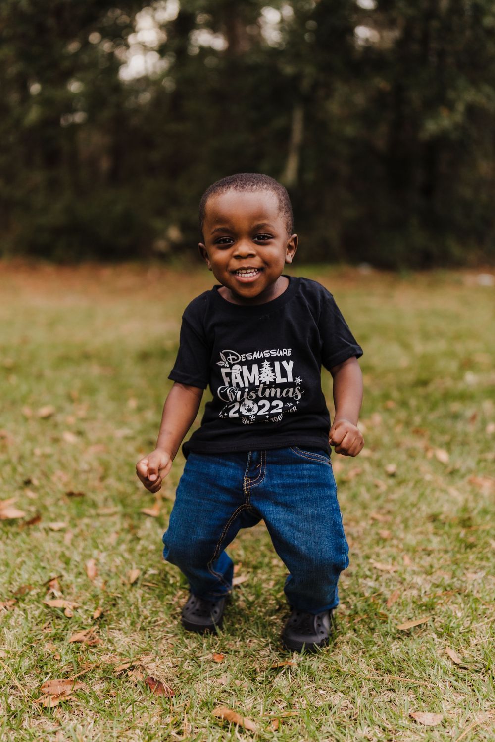 Joyful toddler wearing black t-shirt playing outdoors on grassy field.