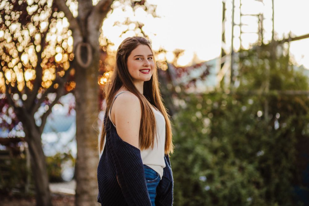 Woman in navy cardigan smiling during golden hour with trees in background.