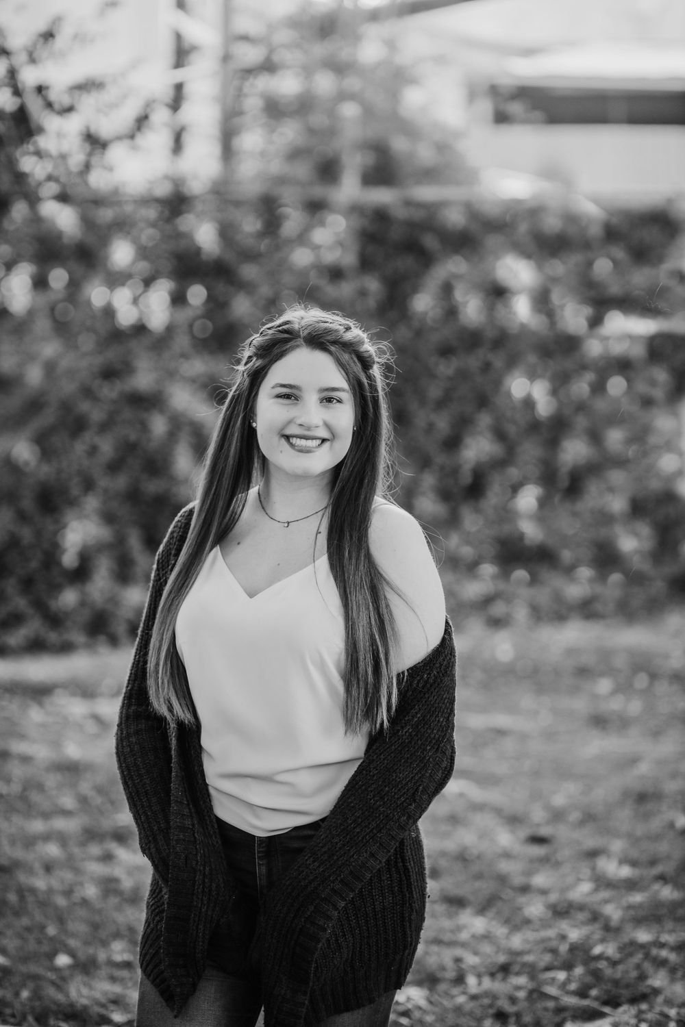 Black and white portrait of woman in white top and dark cardigan smiling outdoors.
