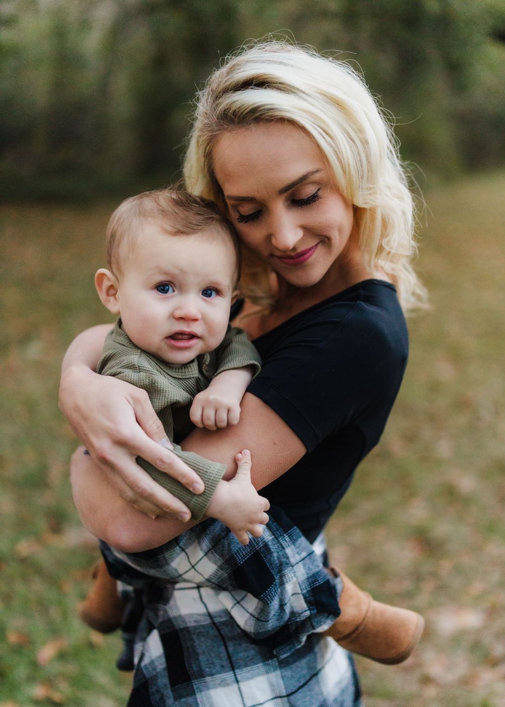 A tender moment between parent and baby in casual attire against a natural outdoor setting.