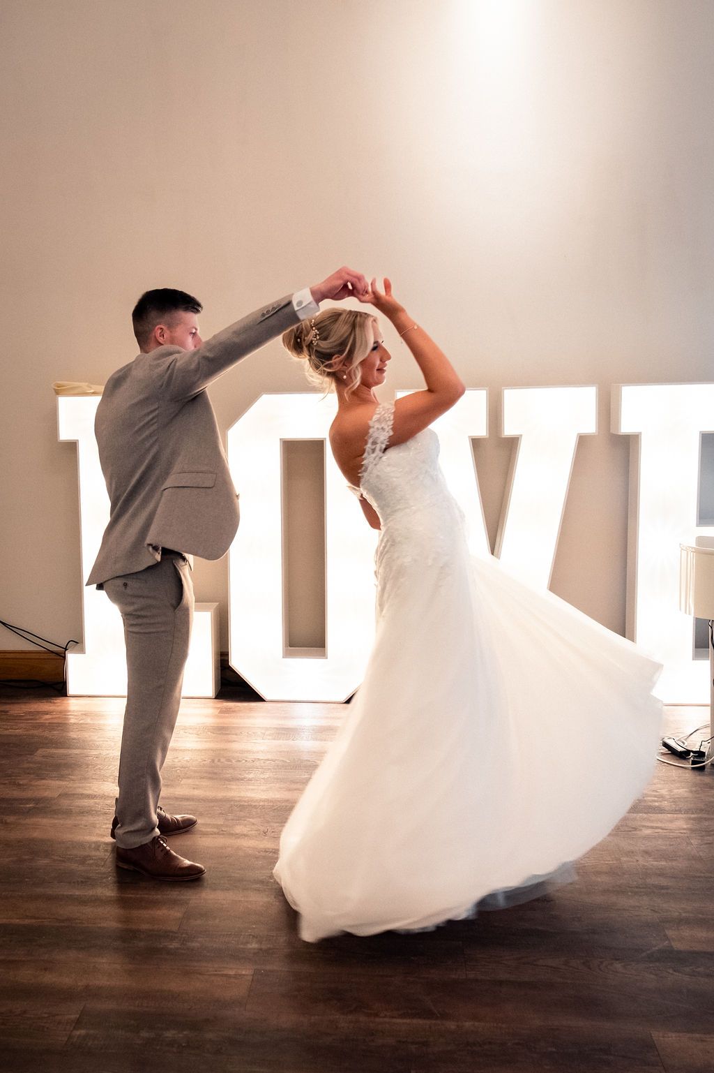 Bride and groom dancing in front of large illuminated "LOVE" letters at their wedding reception.