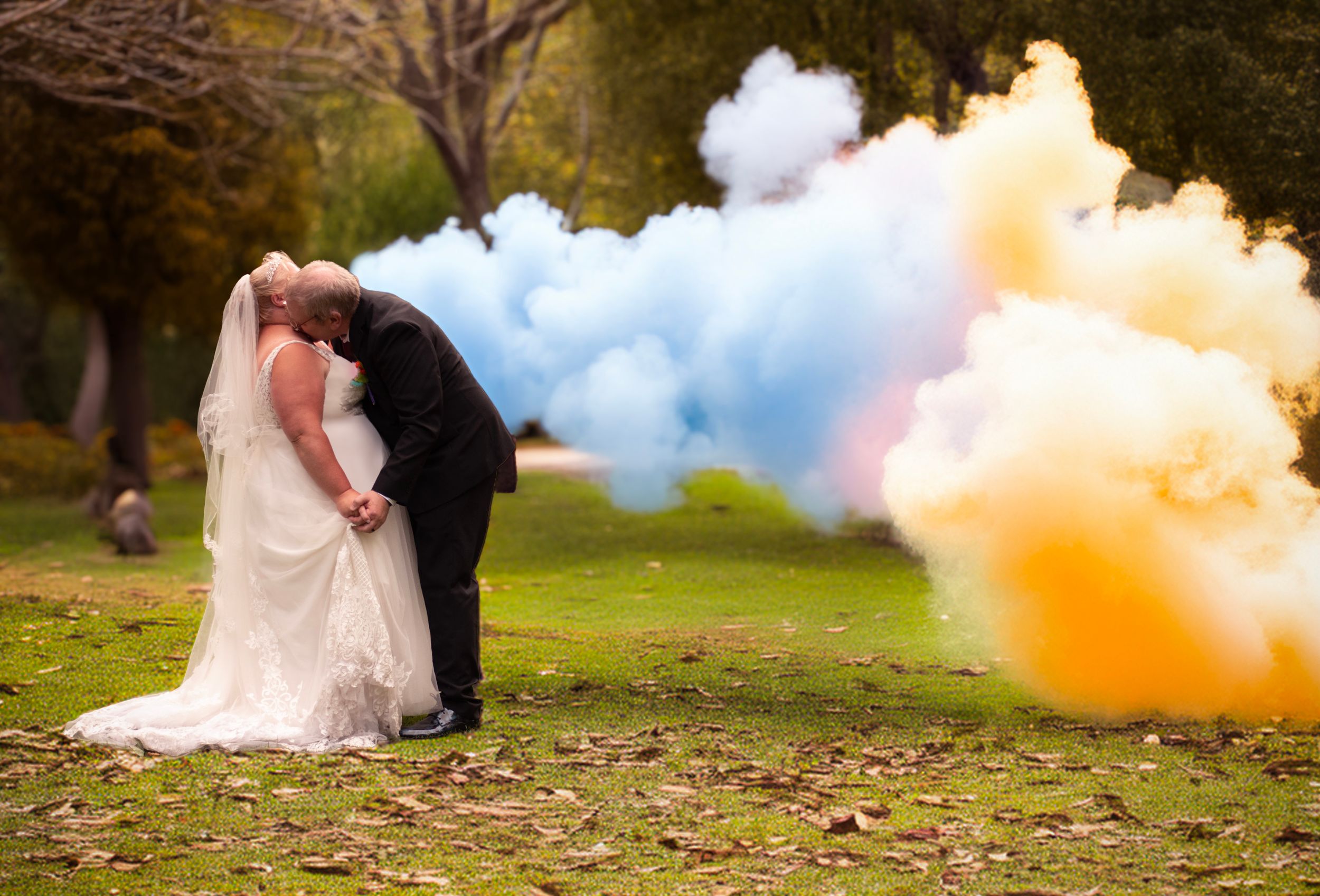 Artistic wedding photo with colorful smoke bombs creating vibrant clouds behind the couple.