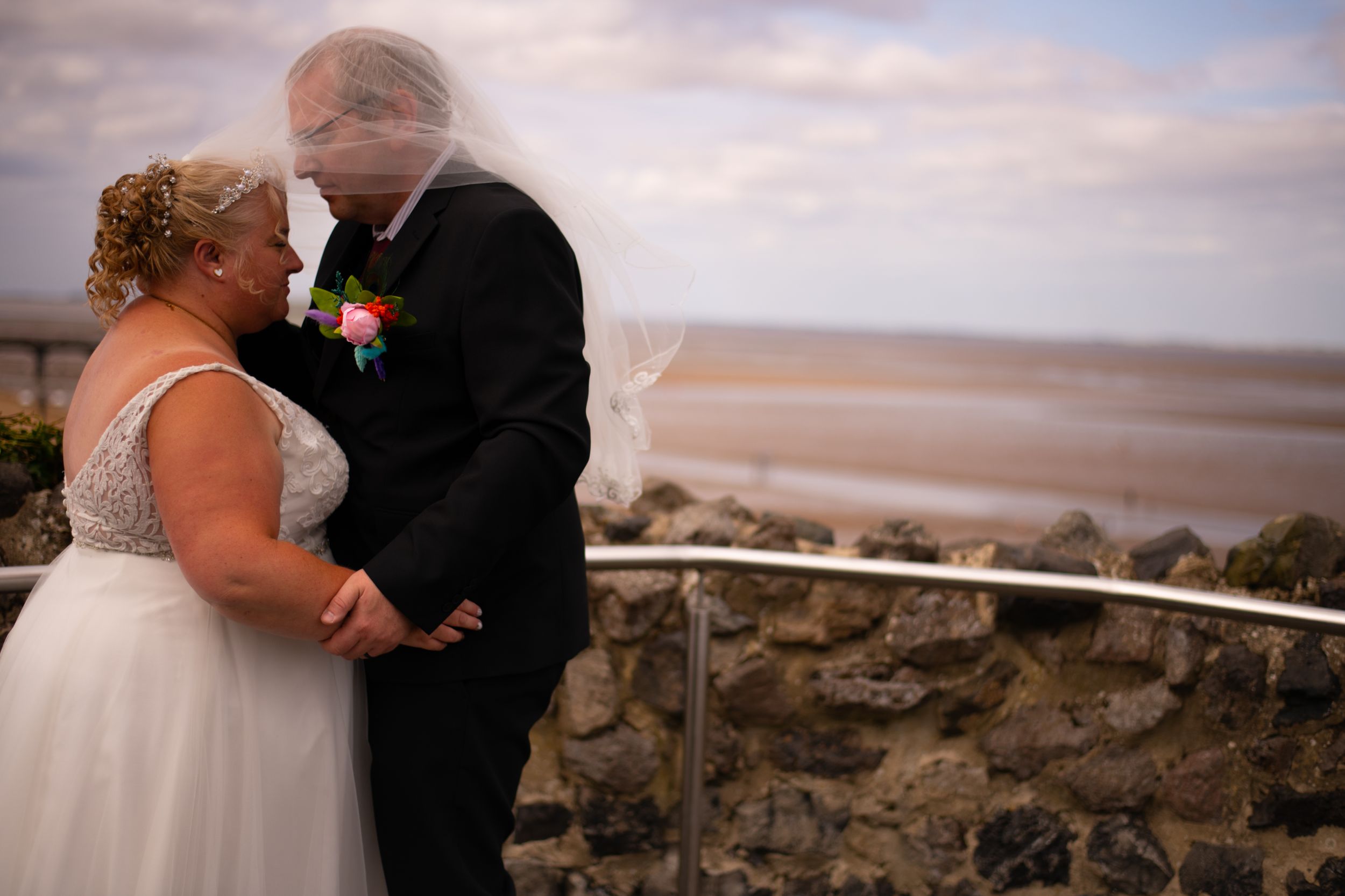A romantic coastal wedding moment with the couple embracing against a scenic ocean backdrop at sunset.