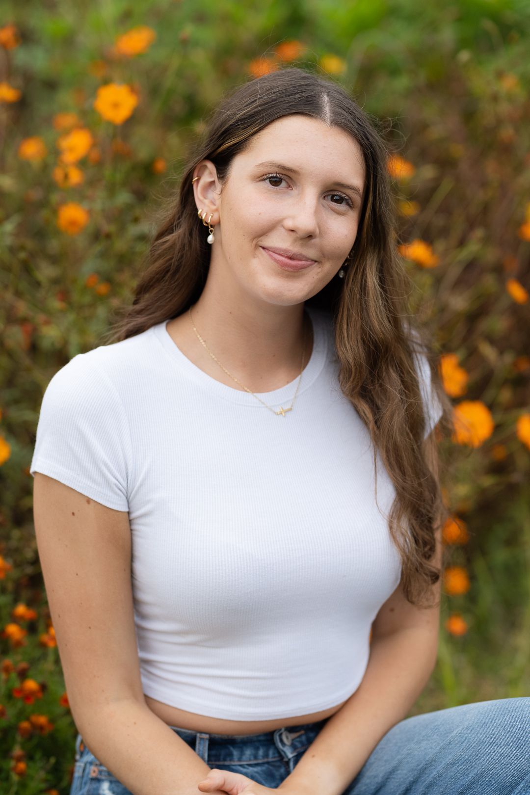 Casual portrait of someone wearing a white crop top and jeans with orange wildflowers in the background.