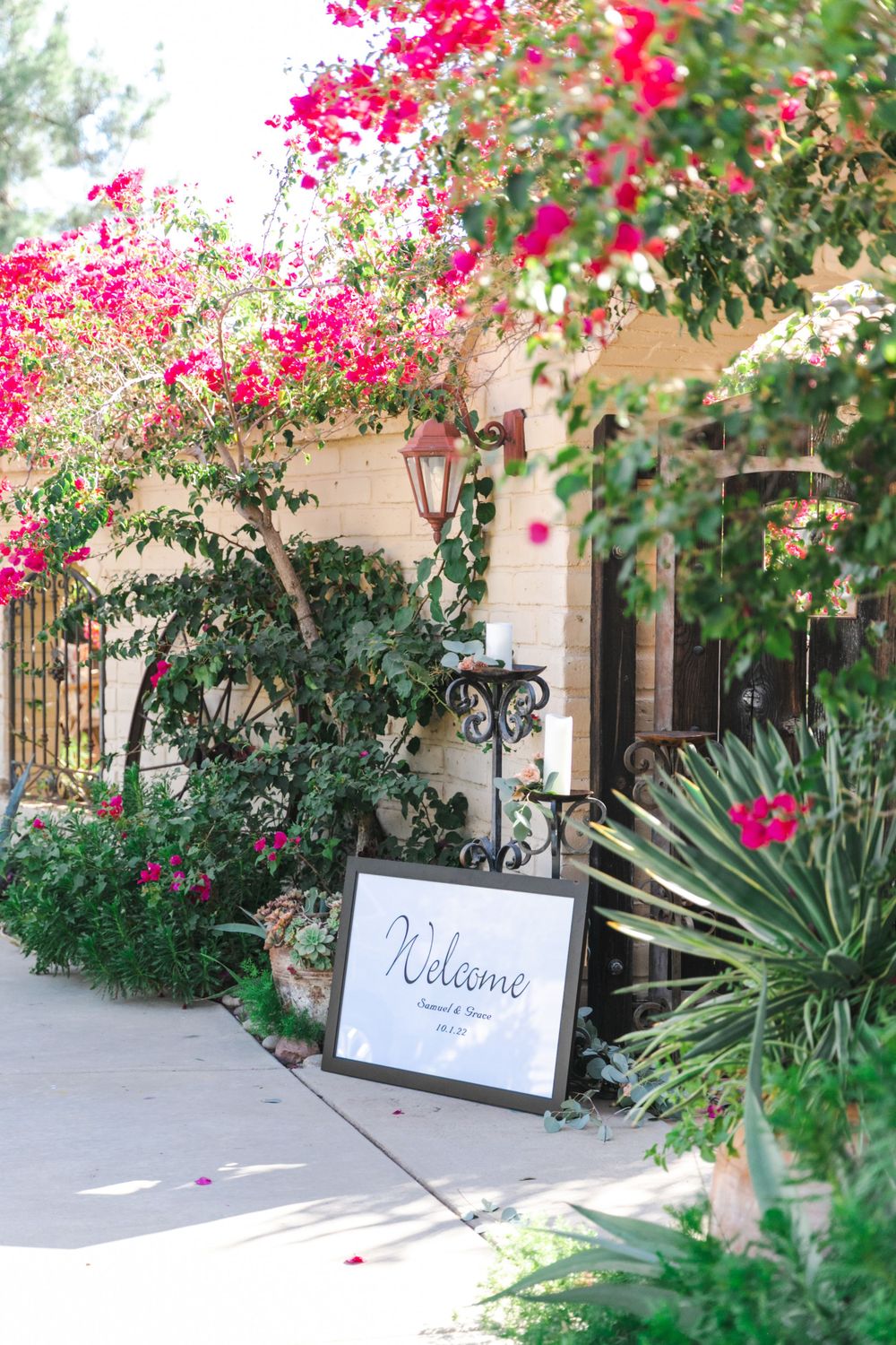 Welcome sign surrounded by vibrant pink bougainvillea at an outdoor wedding venue entrance.