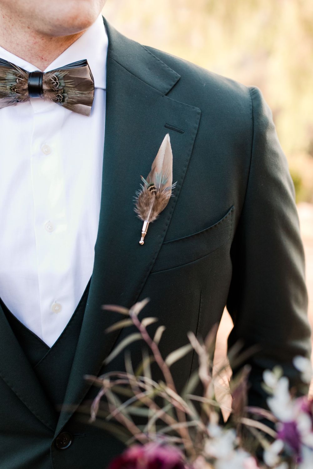 Groom in dark green suit with feather boutonniere and matching feathered bow tie.