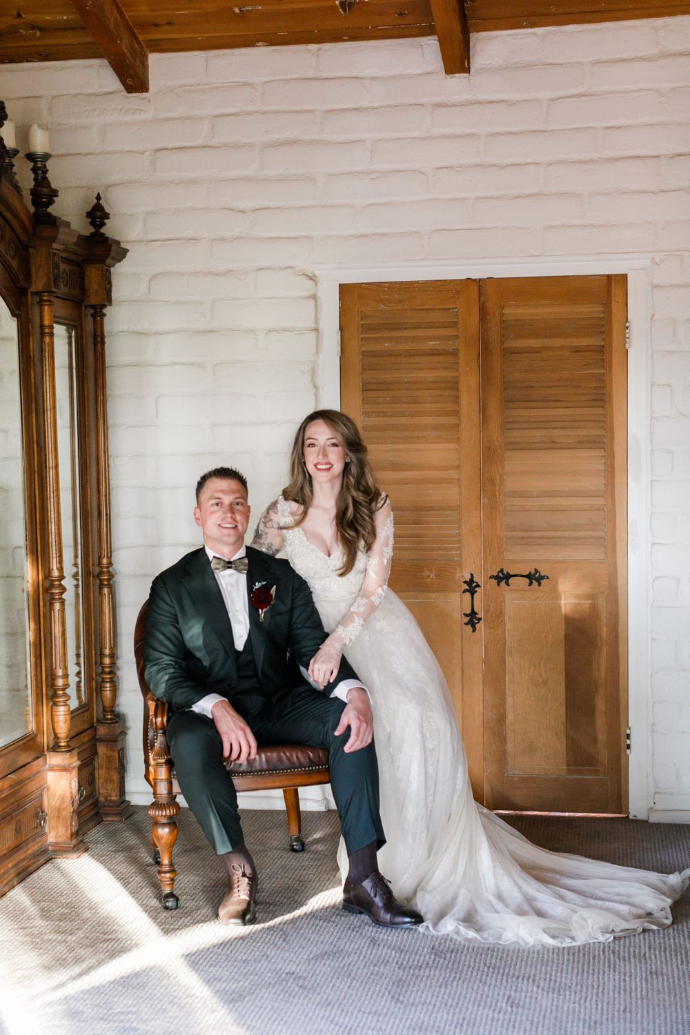 Bride and groom posing together in a bright white brick room with wooden doors.