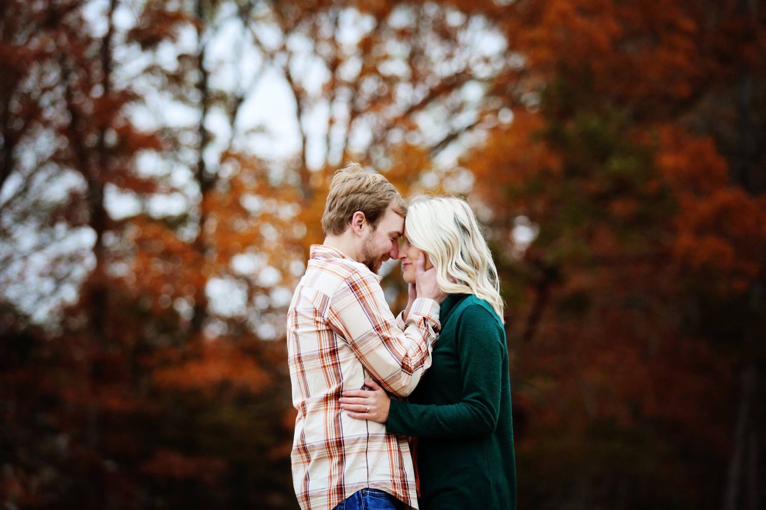Couple embracing in autumn forest with orange foliage backdrop.