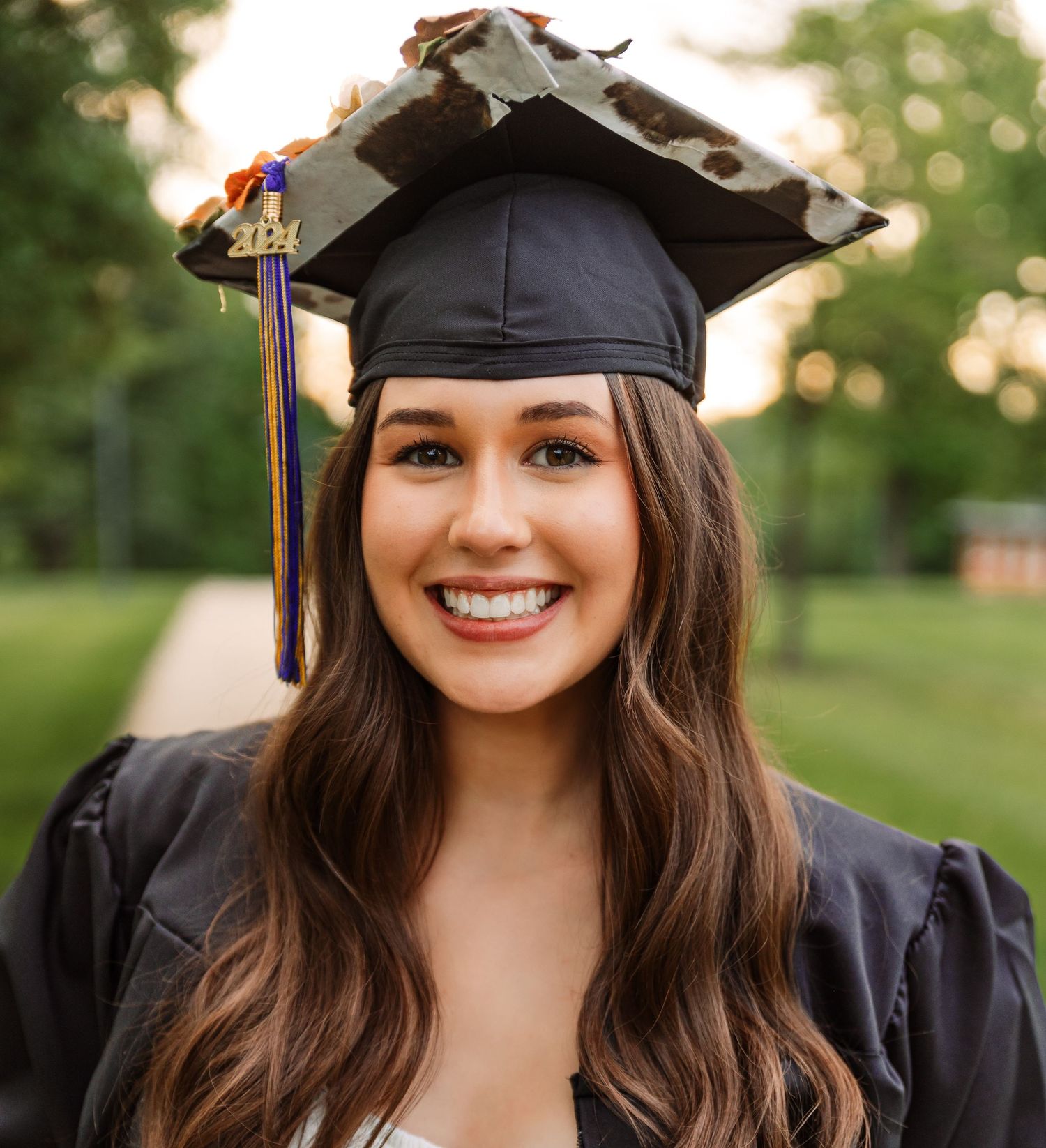 Graduate in black cap and gown poses outdoors during sunset photo session.