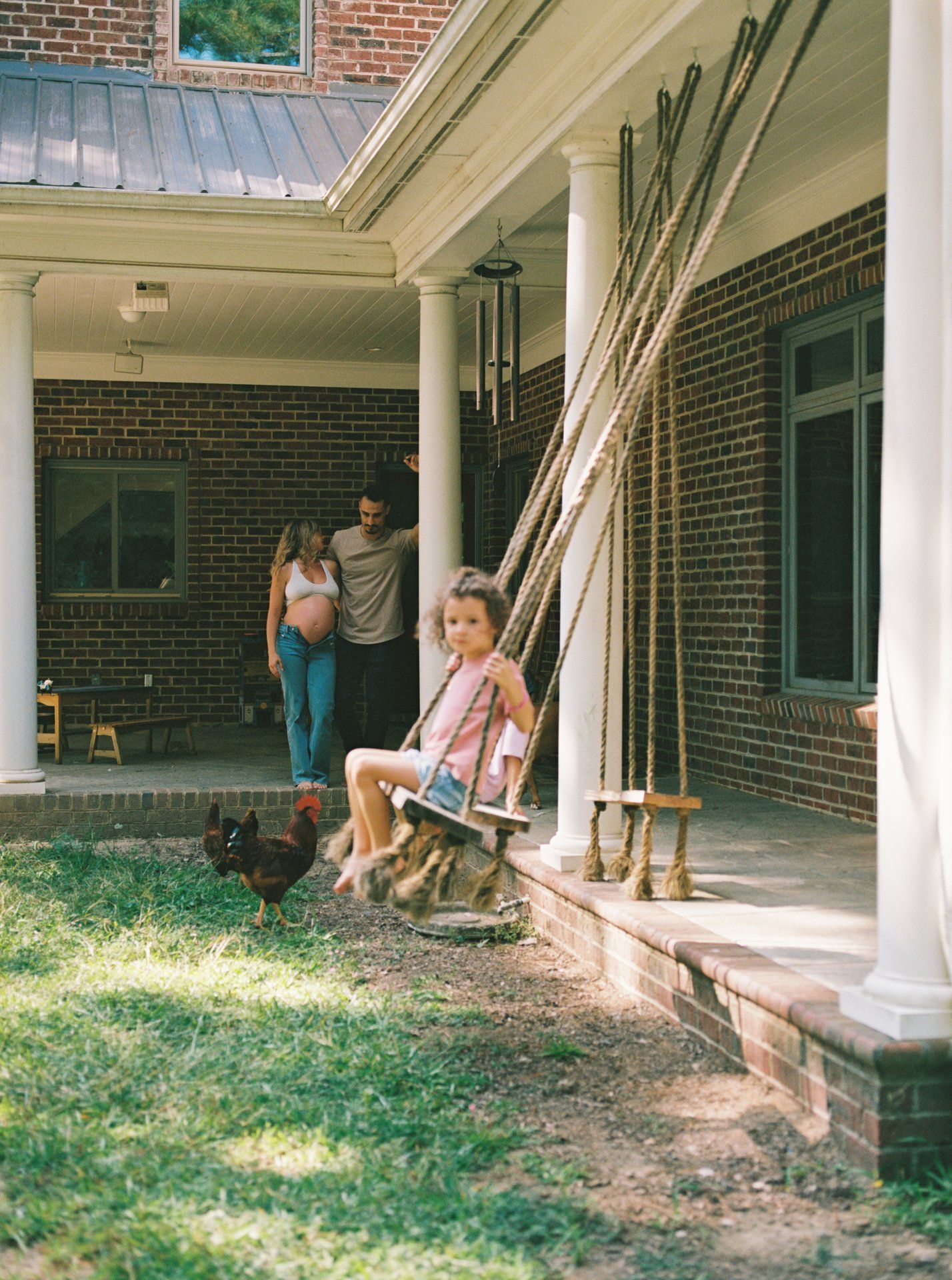 People relax on a covered brick porch with white columns during a sunny day.