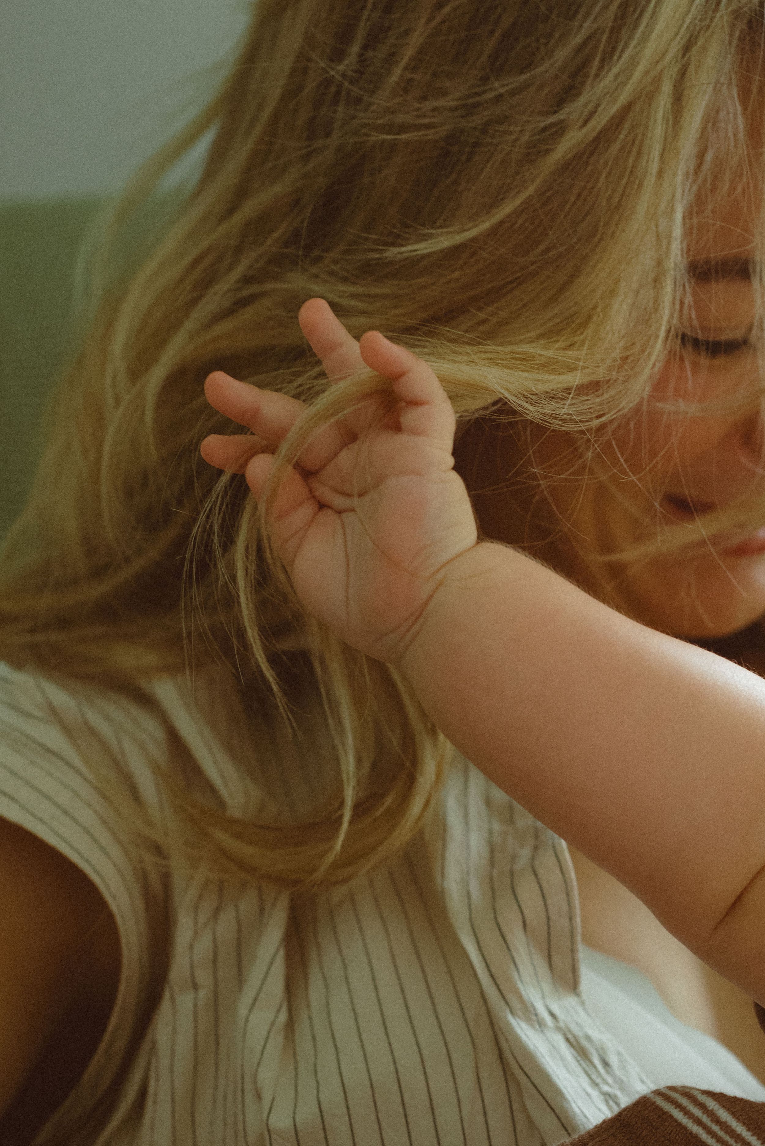 Natural light illuminates blonde hair and a small hand reaching up against a soft white top in a candid moment.