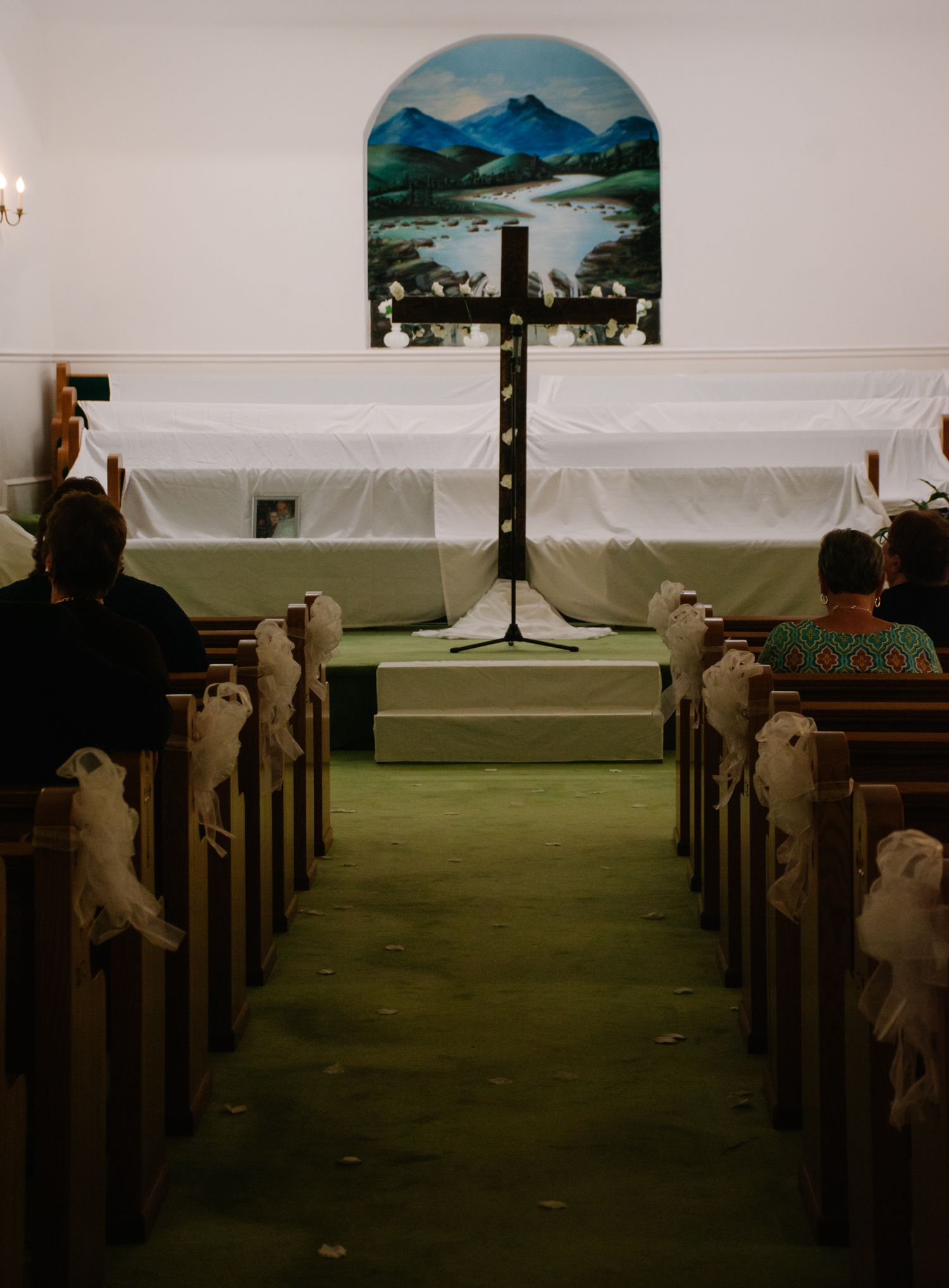 Interior of a church sanctuary with a cross and mountain landscape mural visible through an arched window backdrop.