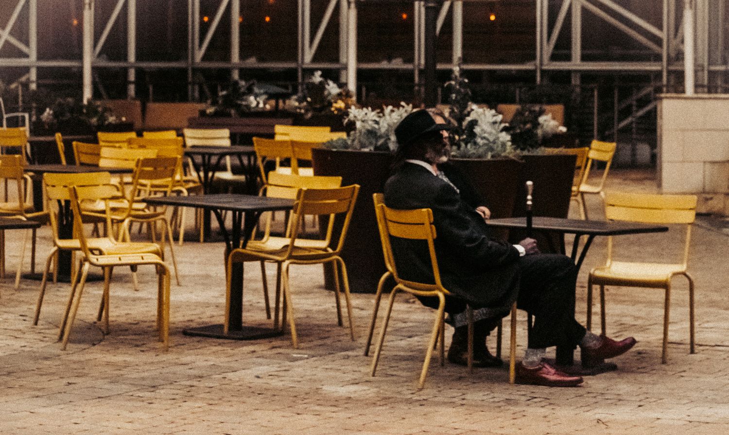 Person sitting alone at yellow chairs in outdoor cafe setting.