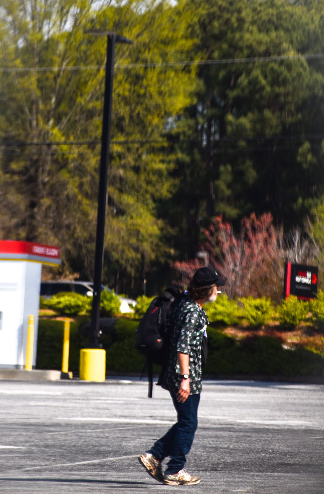 Person in floral shirt walking through parking lot on sunny day.