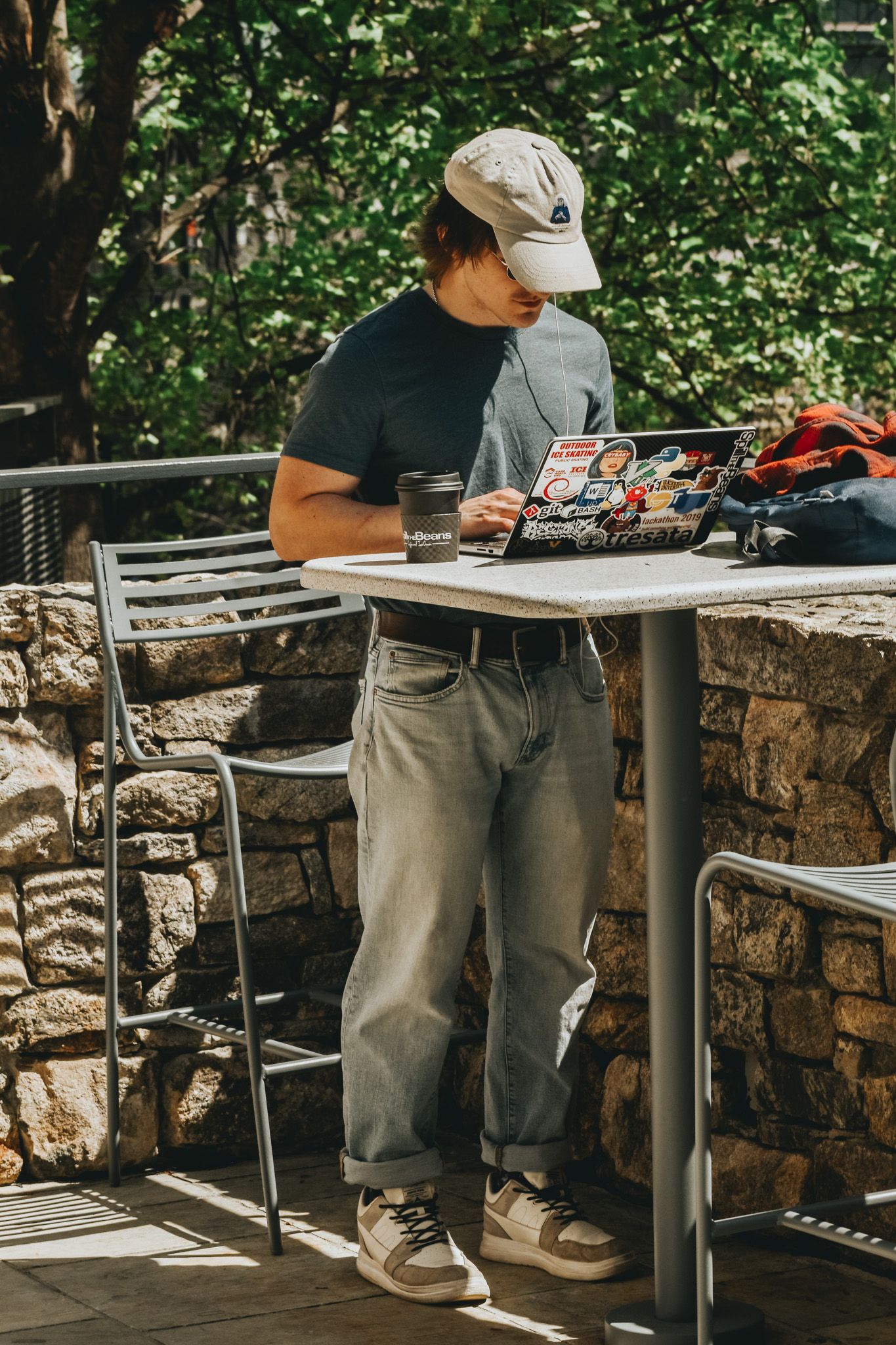 Someone works on a laptop at an outdoor stone patio table.