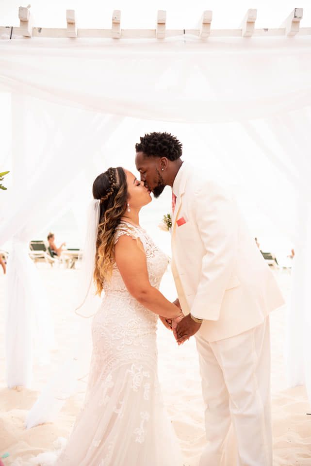 A romantic wedding ceremony moment under a white canopy on a sunny beach.