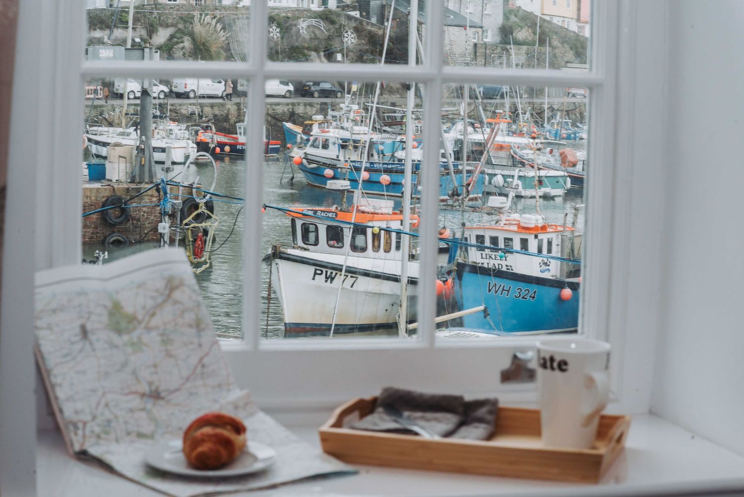 view of boats in mevagissey harbour with coffee, pastry and map in foreground