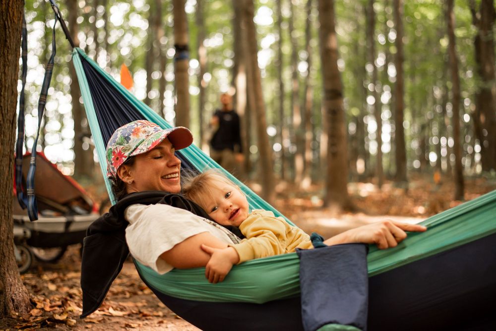 Two people relaxing in a teal hammock among forest trees.