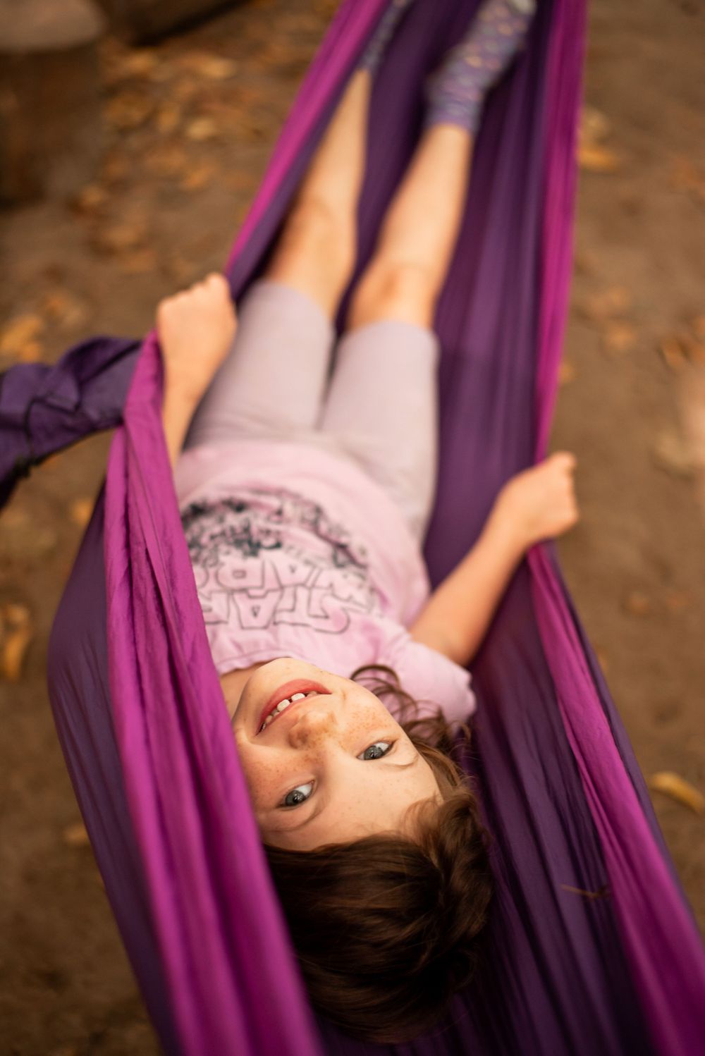 Person lying in a purple hammock among autumn leaves.