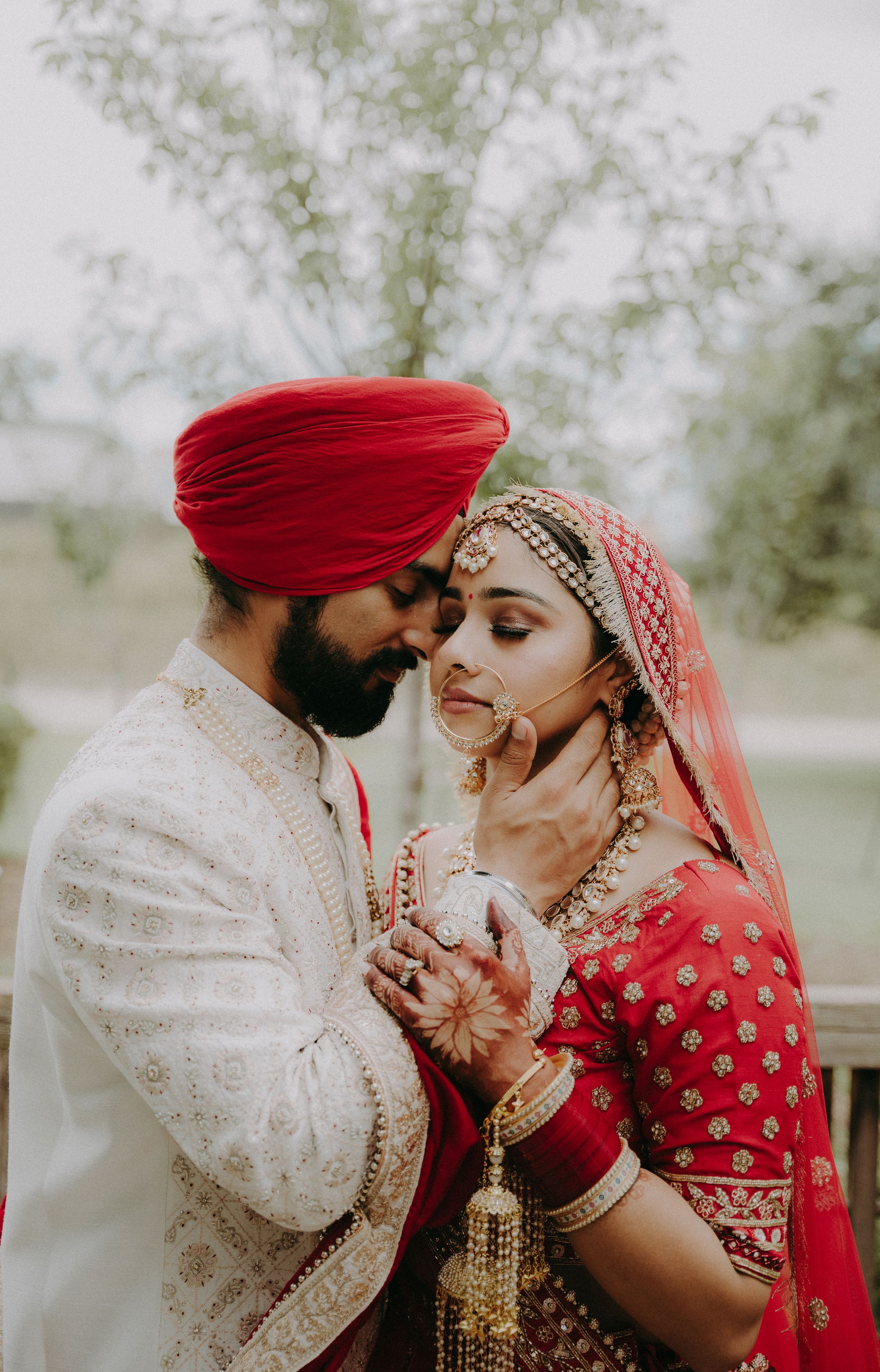 Traditional Indian wedding couple in red and white attire share an intimate moment outdoors.