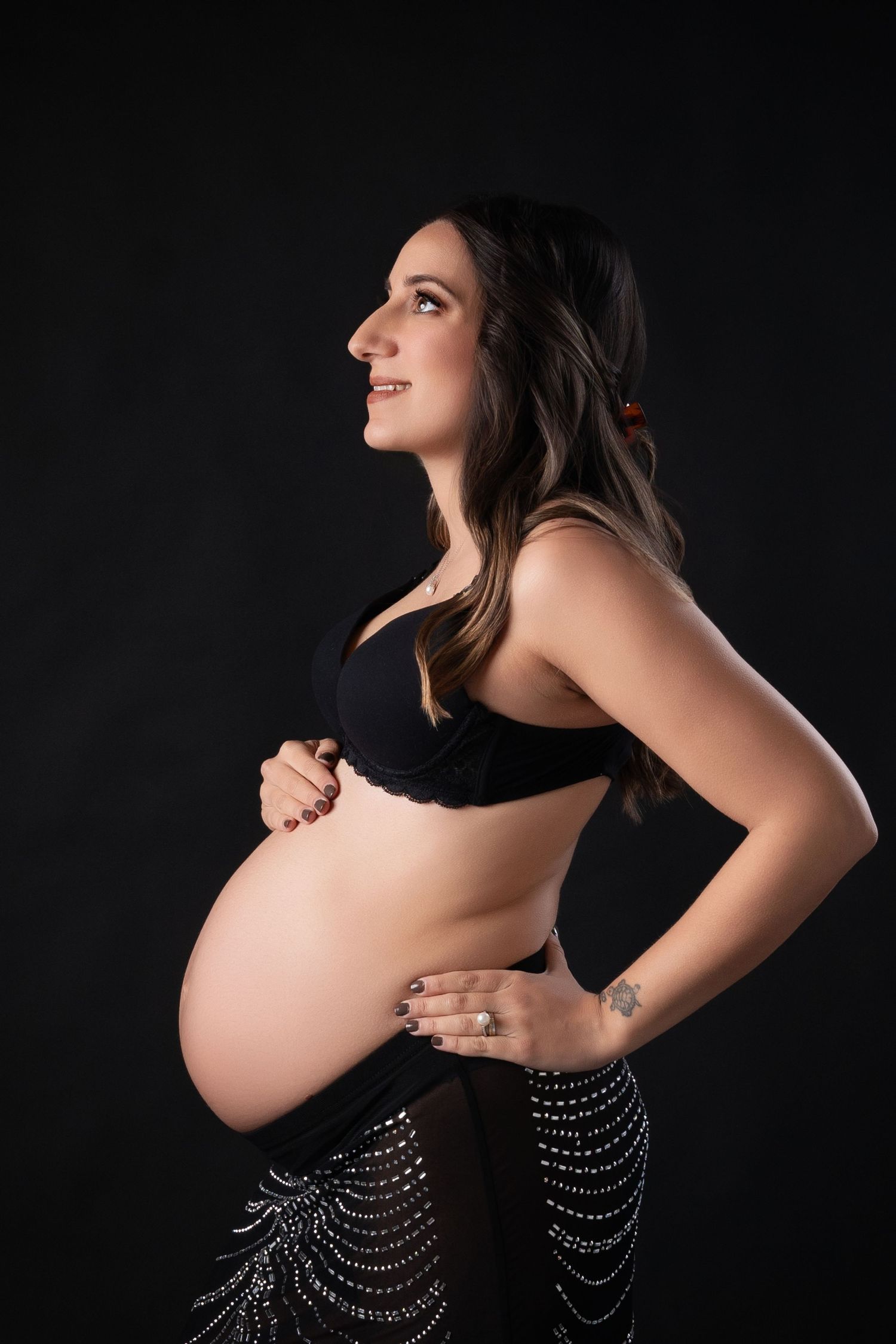Side profile maternity portrait against dark background with sparkly fashion details.