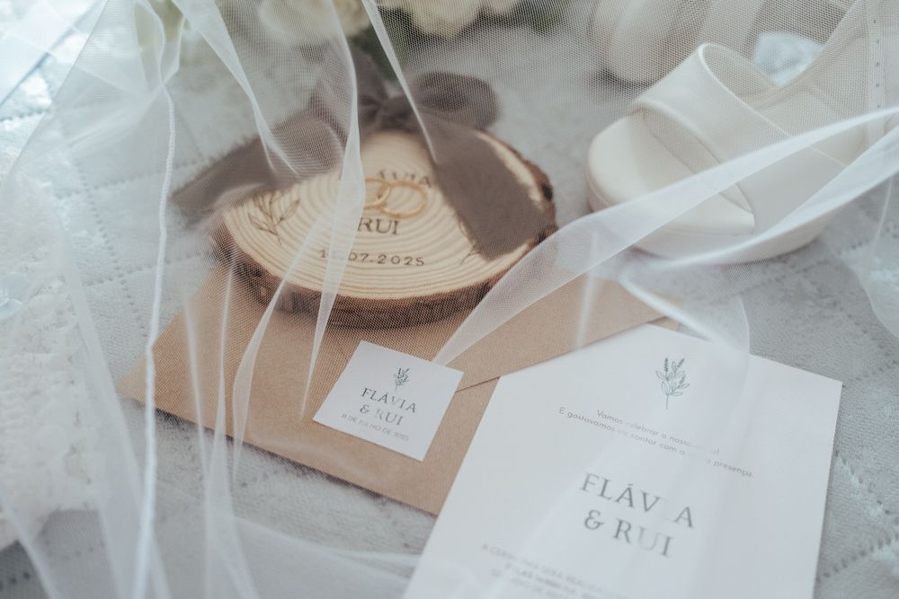 Elegant wedding stationery flat lay featuring invitations and wooden ring dish with couple names Flavia and Rui.