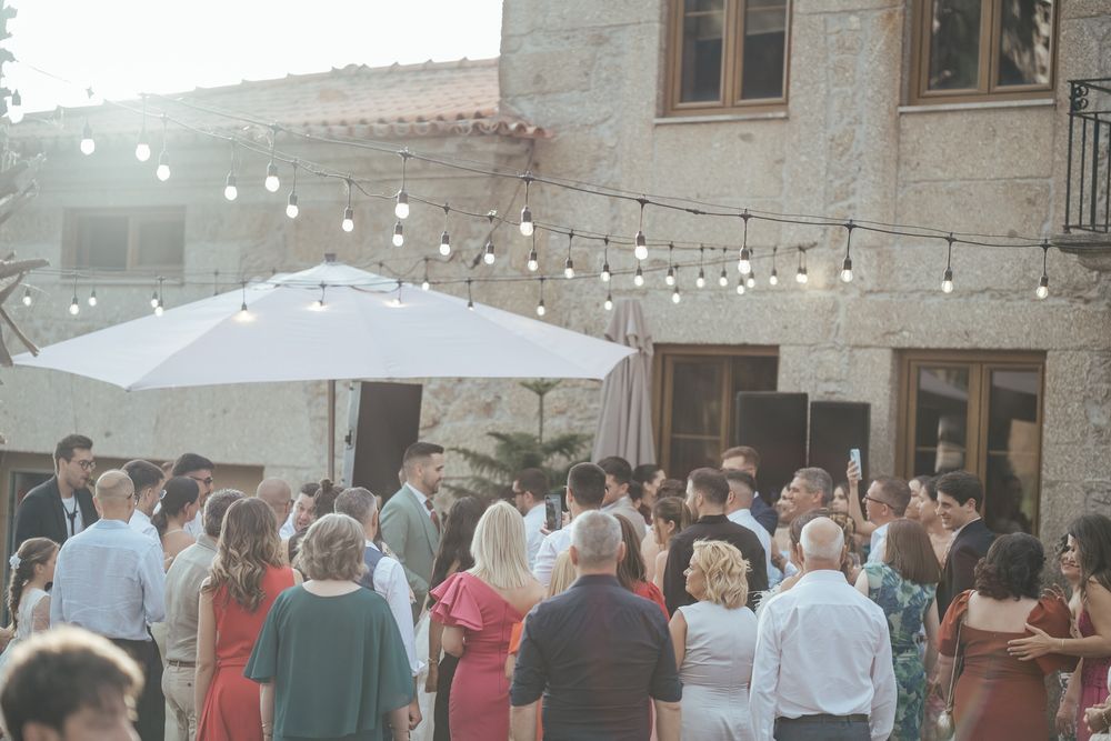 Wedding guests mingling outdoors at a rustic stone venue decorated with warm string lights and a white umbrella.