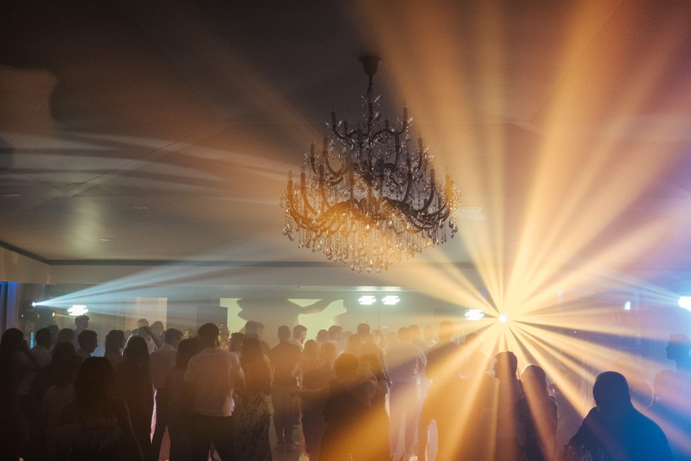 Dramatic wedding reception dance floor with chandelier and golden light rays through misty atmosphere.
