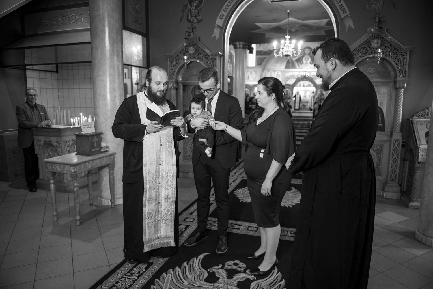 Black and white photo of Orthodox priest performing baptism ceremony with family.