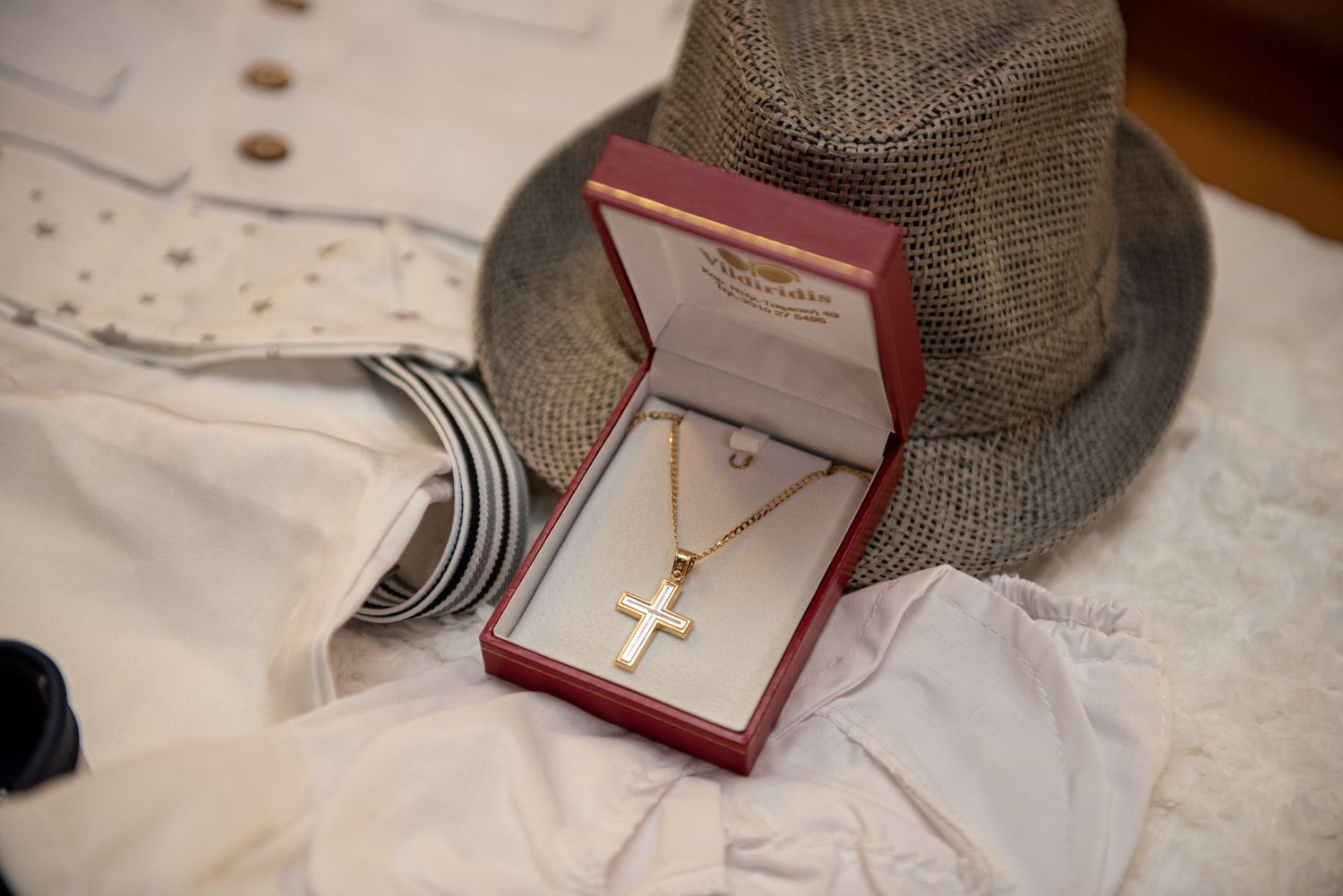 Gold cross necklace in a red jewelry box with baptism outfit and hat.