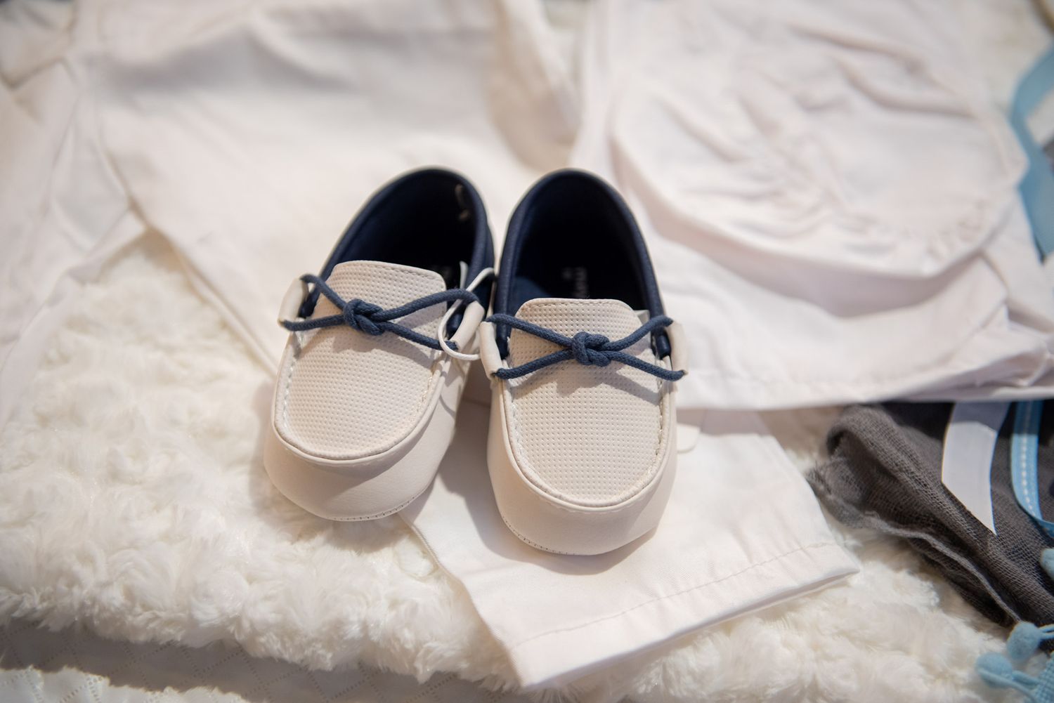 Small white and navy baby boat shoes on a white baptism outfit.