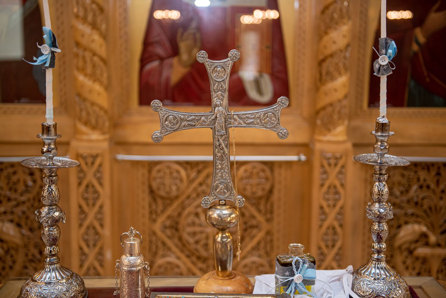Orthodox silver cross and candlesticks on an altar with golden iconostasis in background.