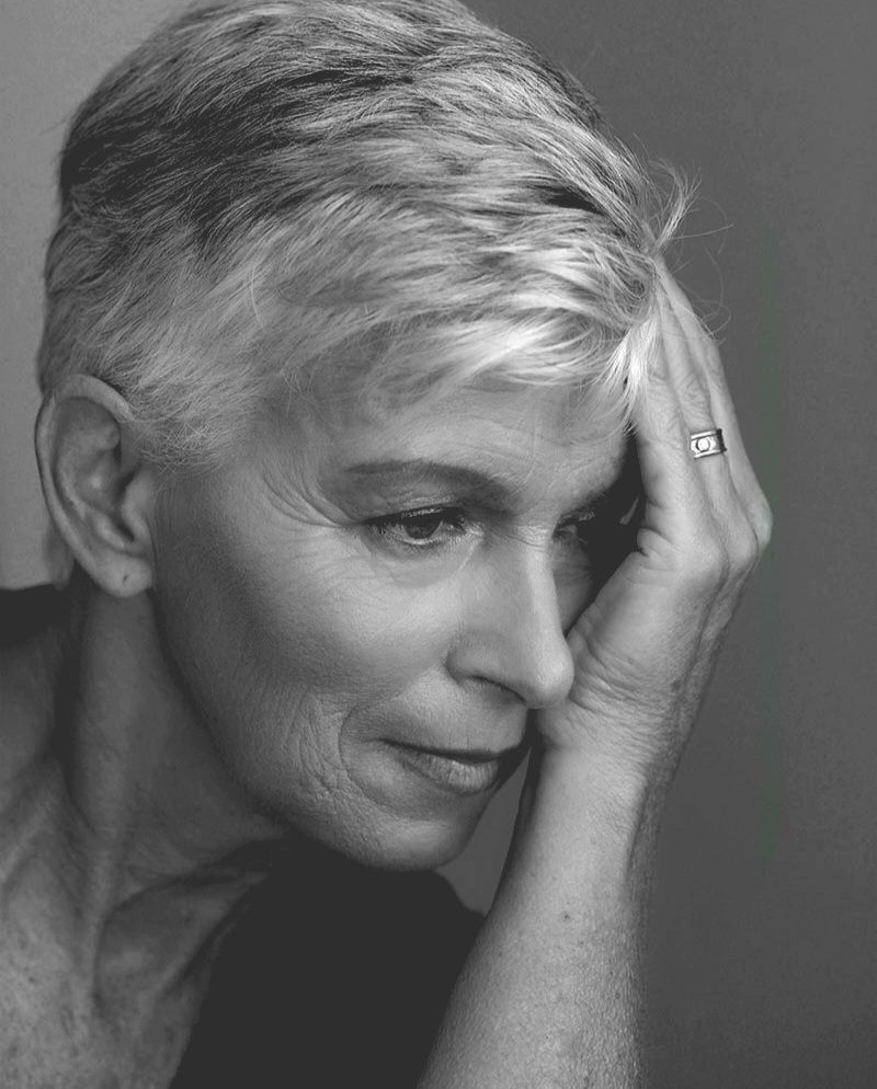 Black and white portrait of an elegant older woman with short gray hair, resting her hand against her face thoughtfully.