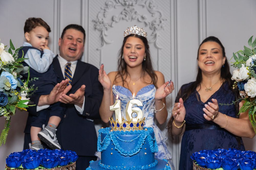 Family celebrating a Sweet 16 birthday party with a blue tiered cake, the birthday girl wearing a crown and blue gown.