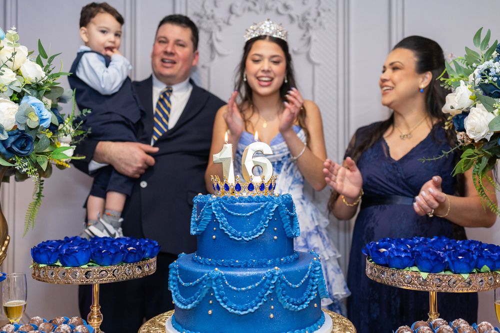 Family celebrating a Sweet 16 birthday party with a blue tiered cake topped with the number 16.