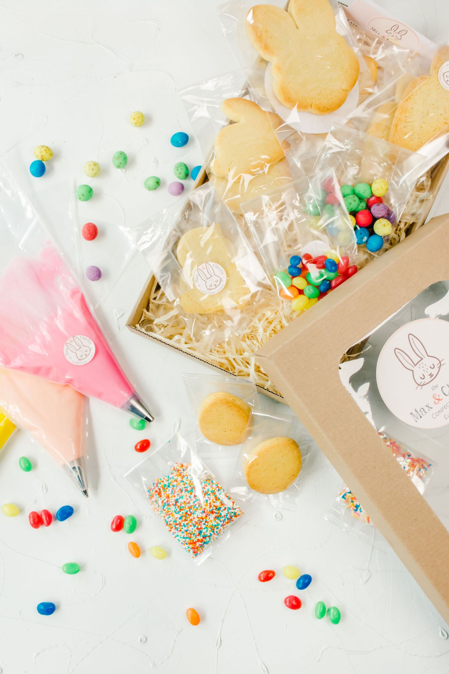 Easter cookie decorating kit with bunny cookies, colorful candies, sprinkles, and pink frosting bag on white surface.