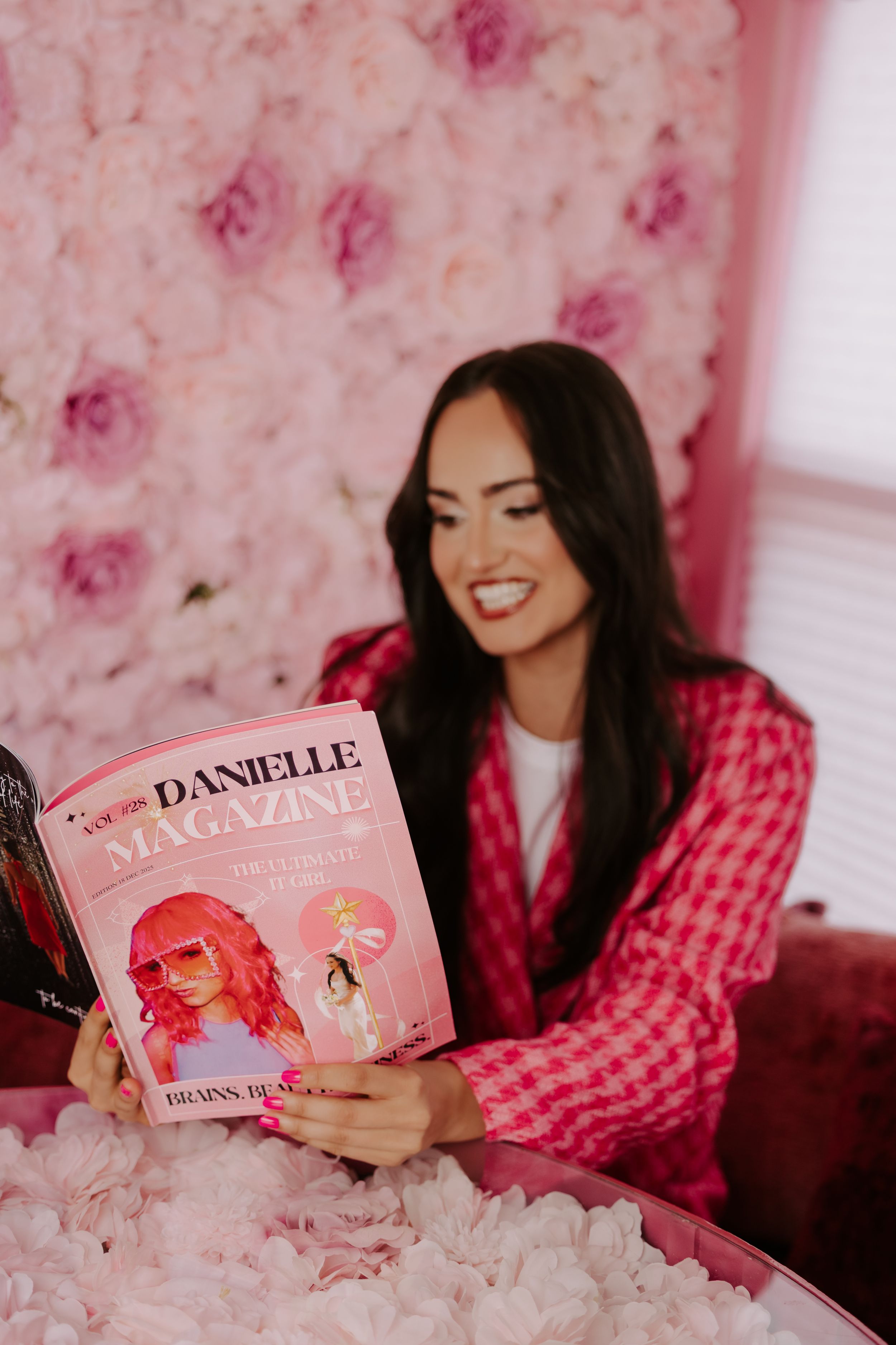 Woman in pink blazer reads Danielle Magazine against a floral pink wall backdrop.