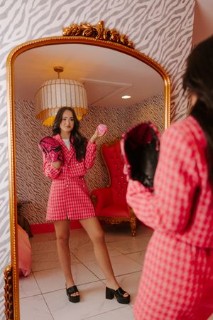 Woman in pink houndstooth suit posing with pink ball in front of decorative gold mirror.