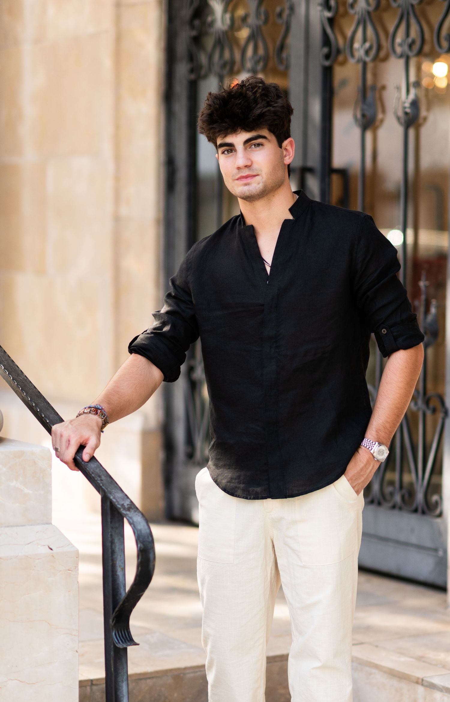 Young man in white short-sleeve shirt and khaki pants leaning on black railing outdoors.