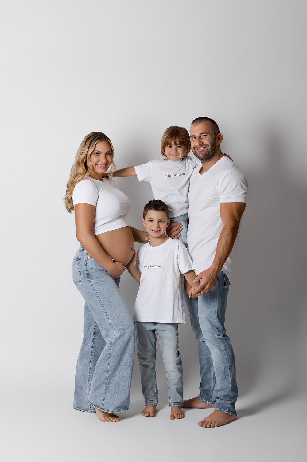 Happy family maternity photo with pregnant mom, dad, and two boys in white tees and jeans.