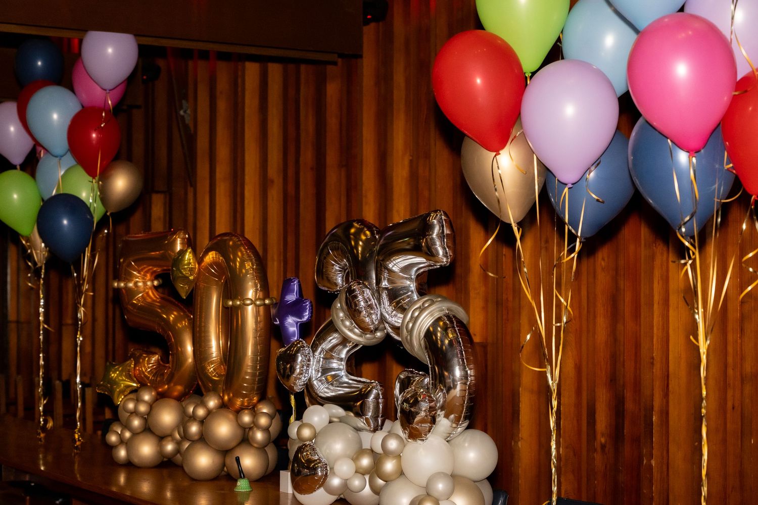 Colorful birthday balloons with gold number balloon decorations against a wooden wall backdrop.