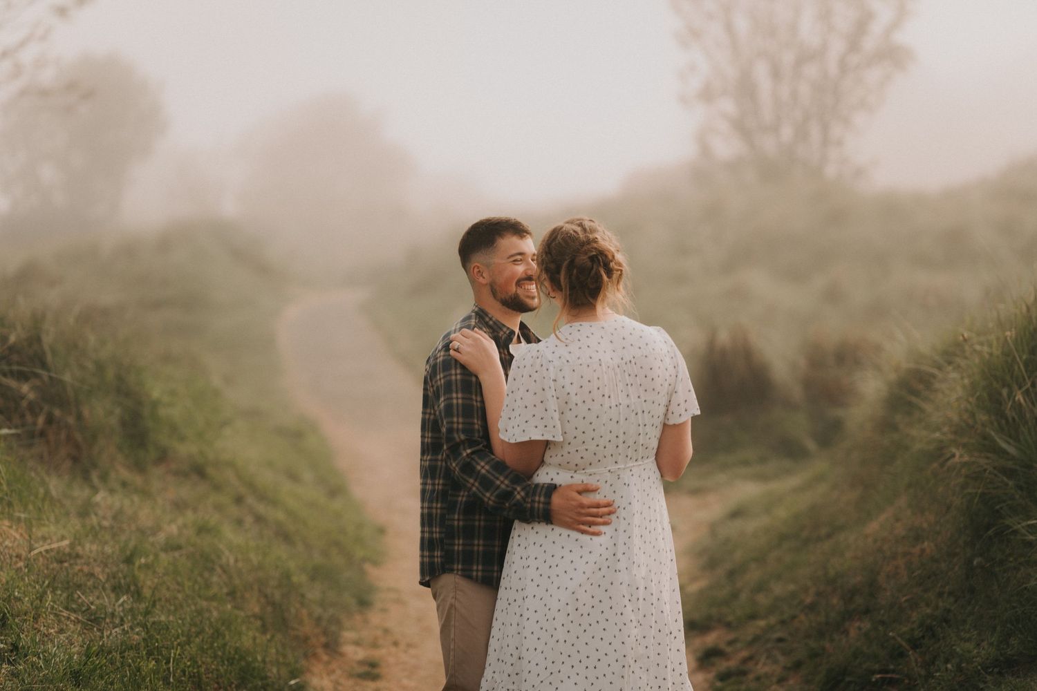 Couple sitting together in a rustic brick bus shelter surrounded by misty green fields on a foggy day.