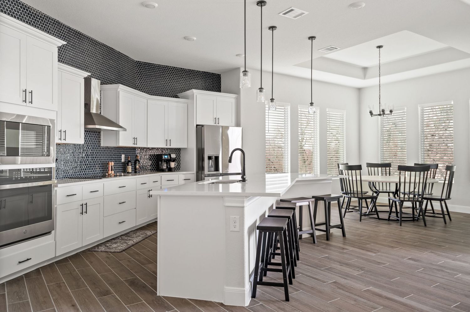 Spacious white kitchen with island seating, modern appliances, and open dining area with wooden floors.