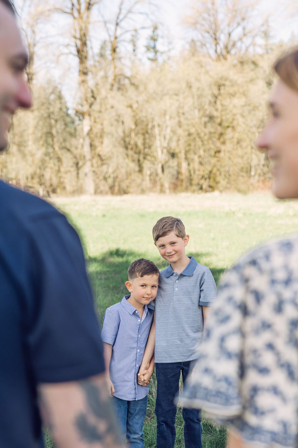 Two young brothers hold hands and smile while their parents stand in the foreground.