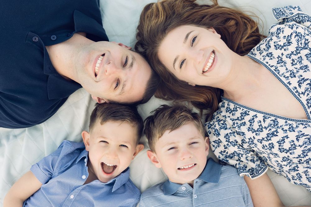 Aerial view of happy family of four lying together smiling, two parents and two young boys in blue shirts.