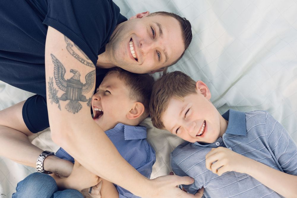 A smiling father lies with his two laughing sons in a fun overhead portrait.