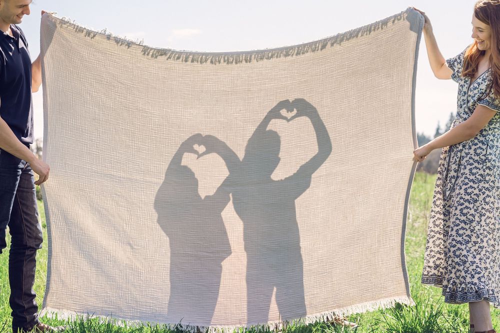 Couple holding a blanket showing silhouettes of two children making heart shapes with their hands.