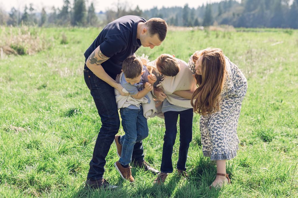 Happy family of four sharing a joyful group hug and laughing together on a bright green lawn.