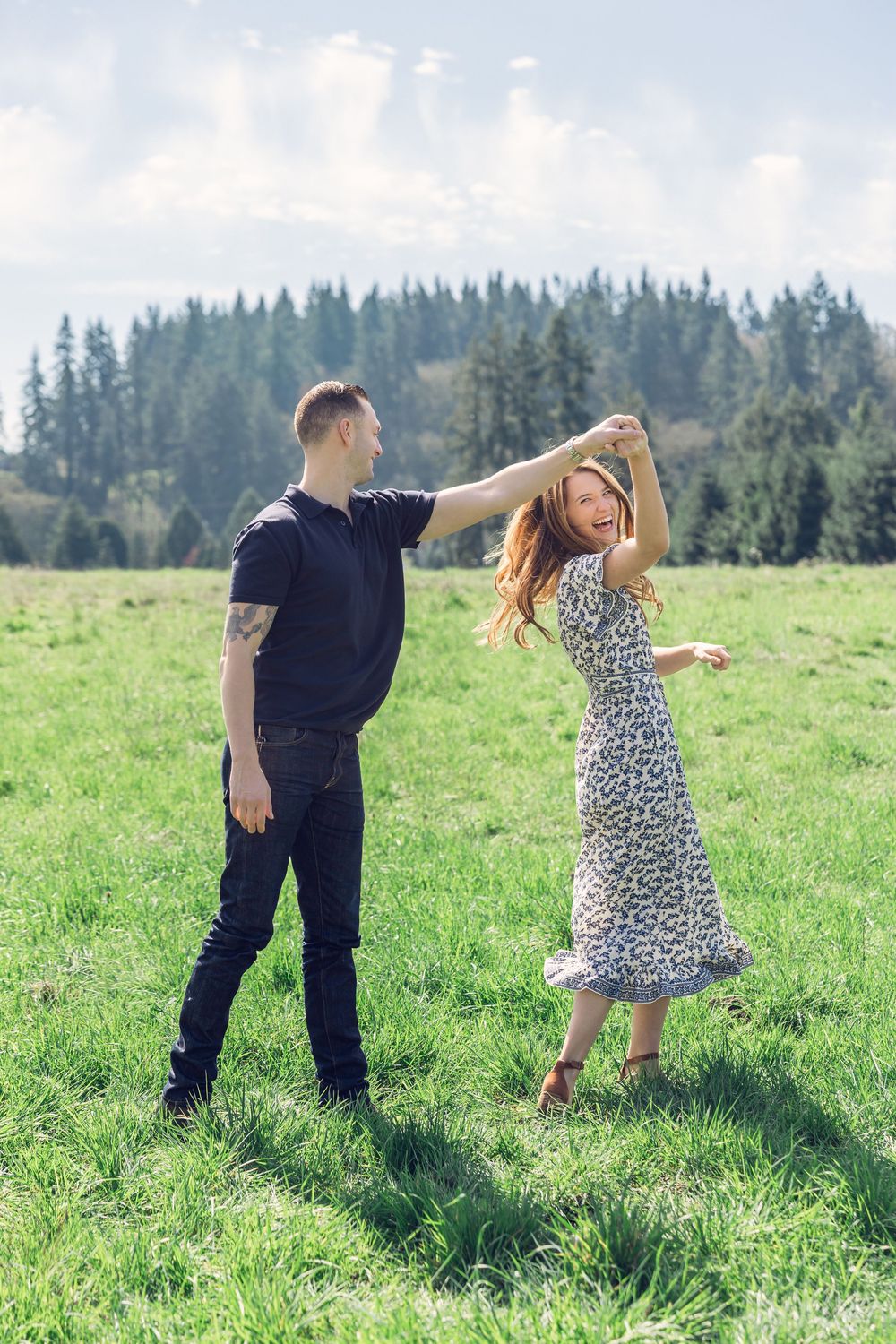 Romantic couple dancing together in a sunny green meadow surrounded by tall pine trees in background.