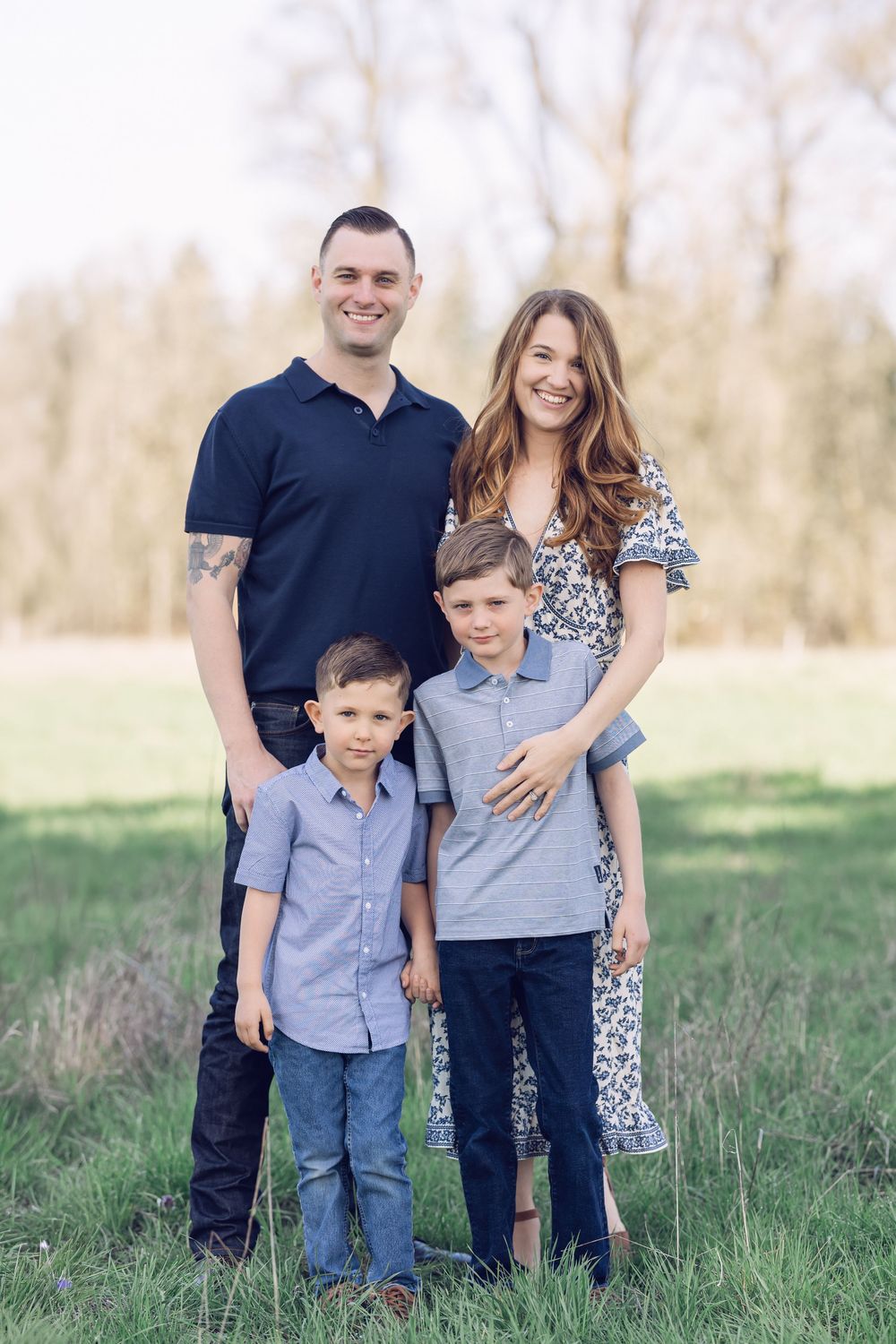 Happy family of four poses together smiling in a lush green field during a spring outdoor photo session.